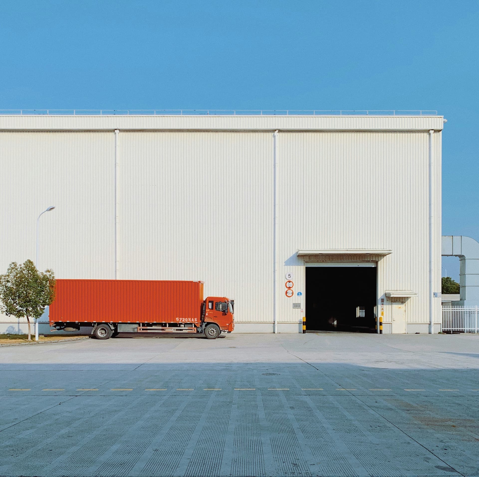 Orange truck waiting outside white warehouse. Credit: Han Chenxu, Unsplash.