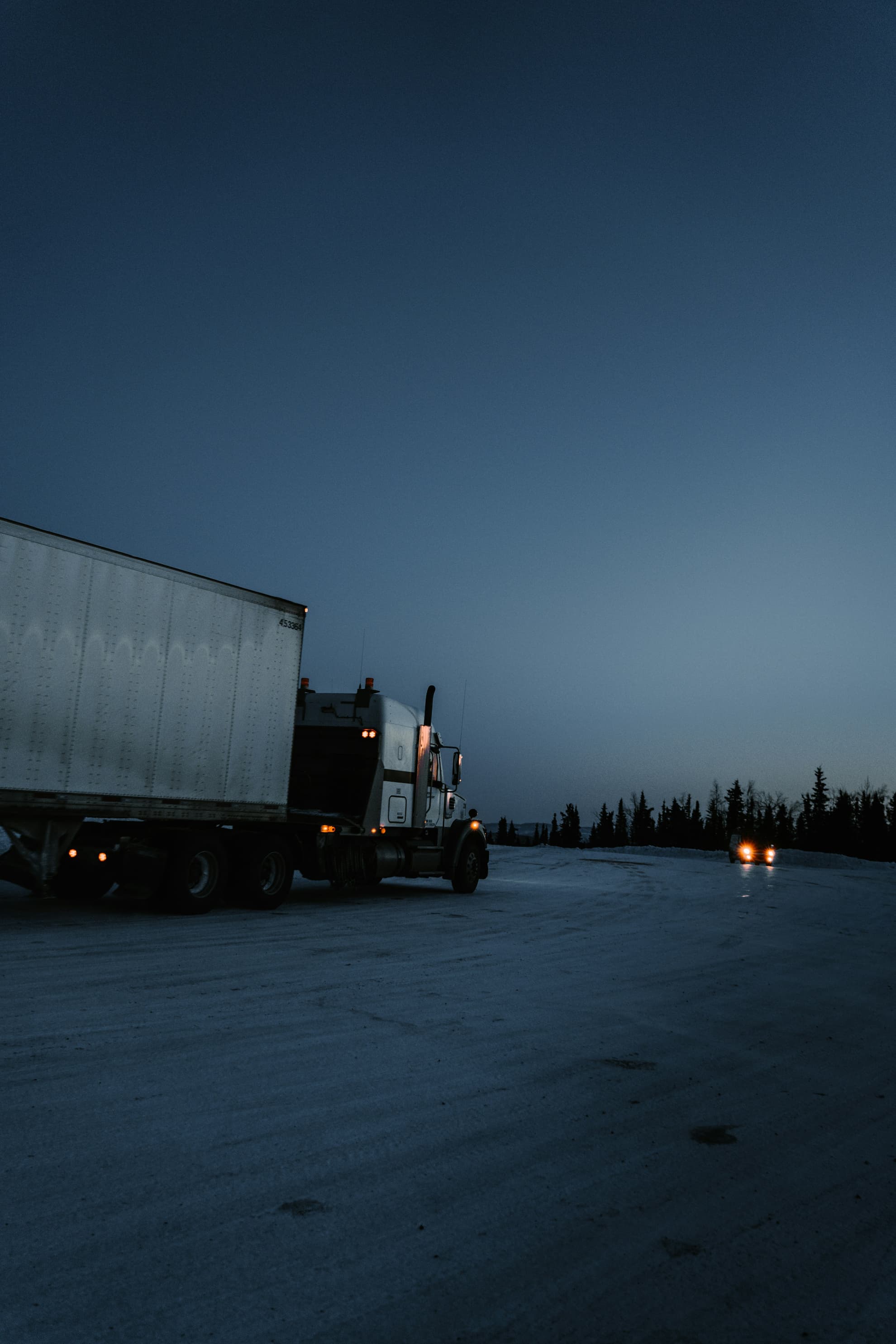 A semi-truck parked on a snowy road at dusk. Credit: ZHENYU LUO, Unsplash.