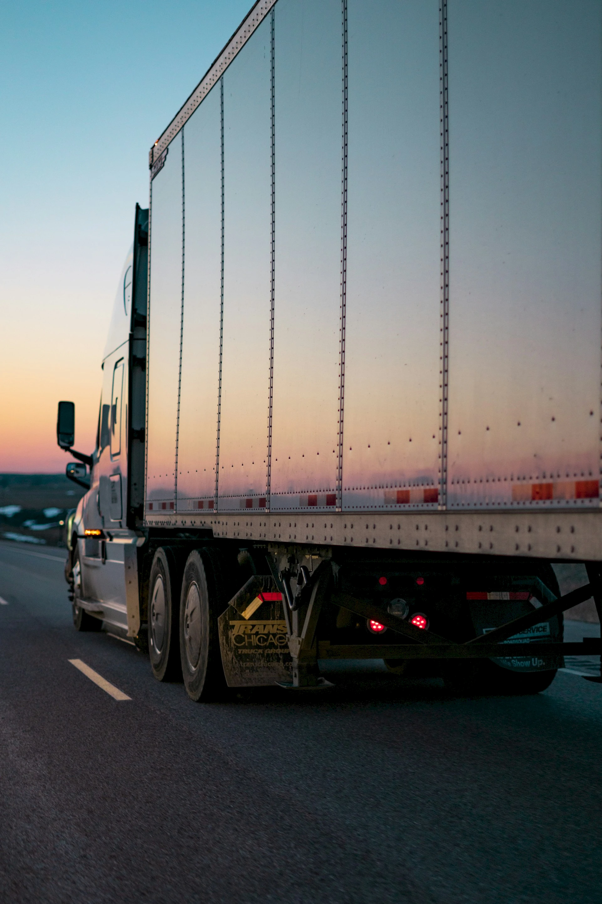 Semi-truck with reflective trailer on the highway at sunset. Credit: Caleb Ruiter, Unsplash.