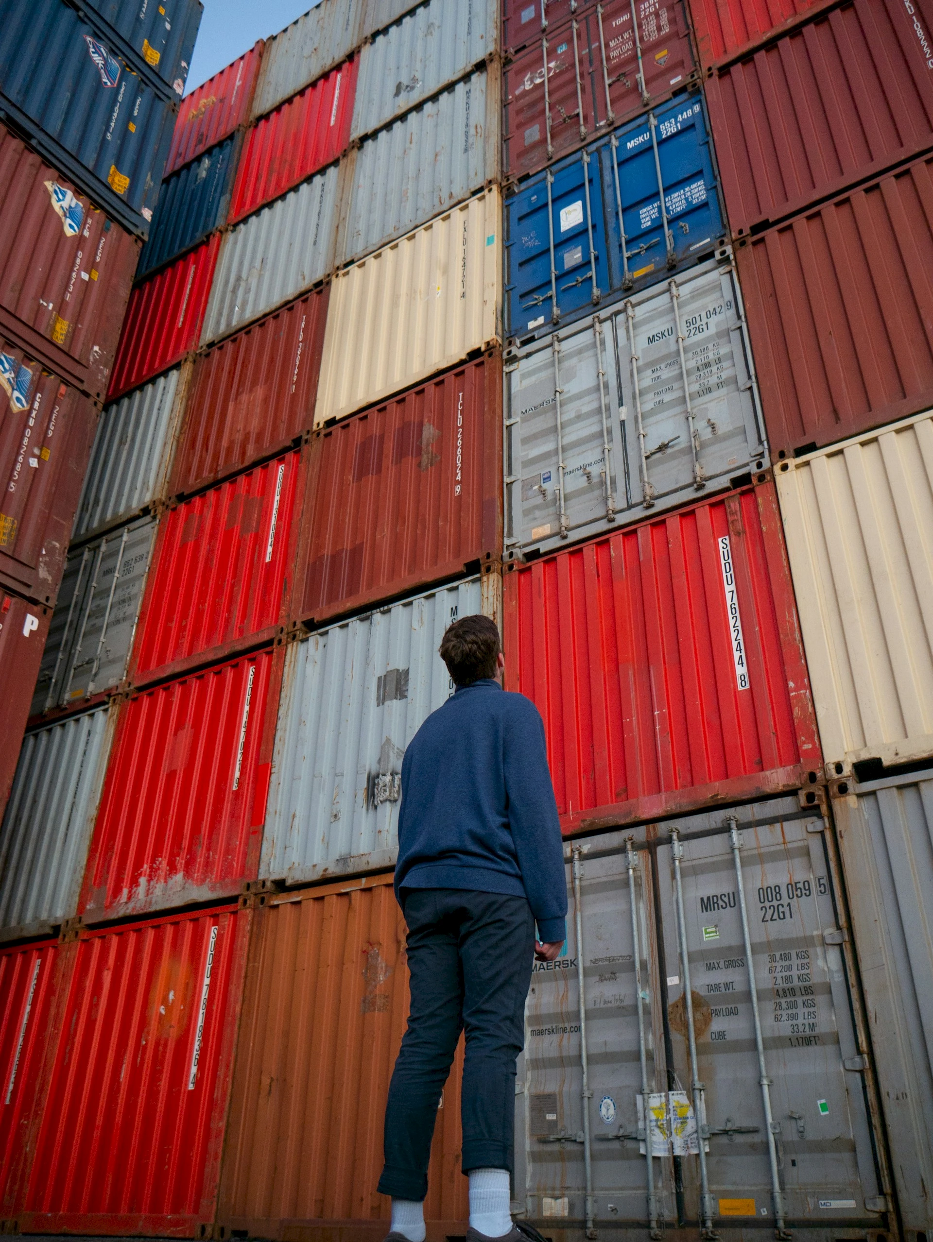 Person looking up at stack of shipping containers. Credit: Pat Whelen, Unsplash